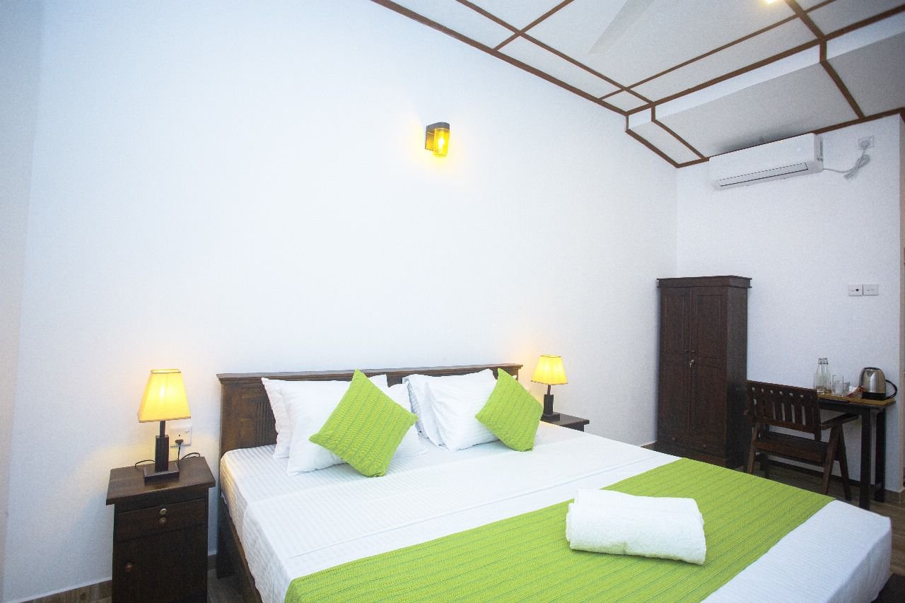 A Deluxe Double Room with green accent cushions, air conditioning and a writing desk