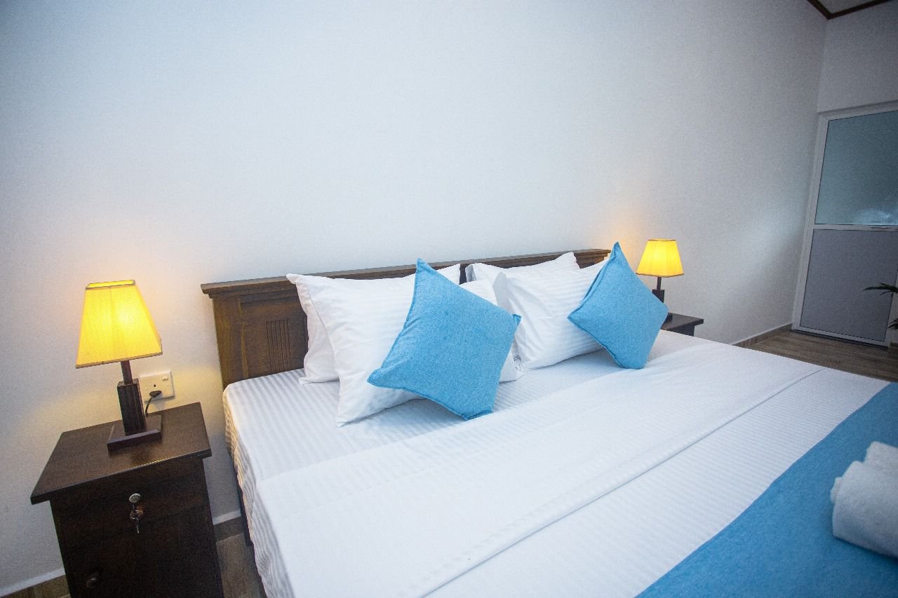 Close view of the Deluxe Double Room's bed, dressed in white linen and blue cushions